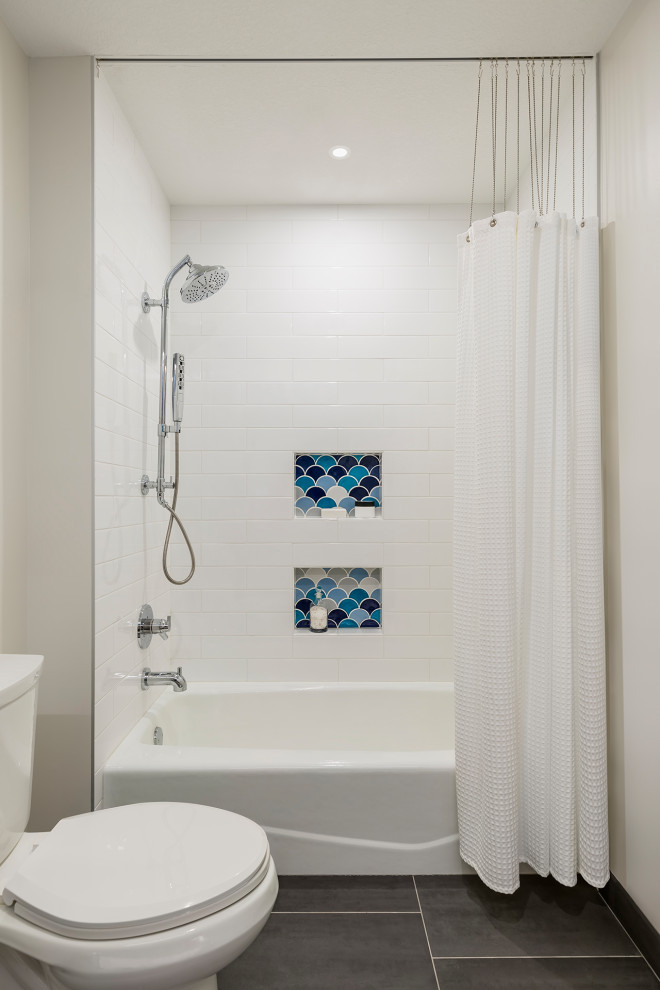 This is an example of a small modern kids bathroom in Minneapolis with flat-panel cabinets, medium wood cabinets, an alcove tub, a shower/bathtub combo, a two-piece toilet, multi-coloured tile, ceramic tile, white walls, porcelain floors, an undermount sink, engineered quartz benchtops, grey floor, a shower curtain, white benchtops, a niche, a double vanity and a floating vanity.