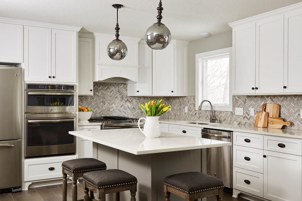 Design ideas for a transitional l-shaped kitchen in Minneapolis with an undermount sink, shaker cabinets, white cabinets, multi-coloured splashback, stainless steel appliances, with island, brown floor and beige benchtop.