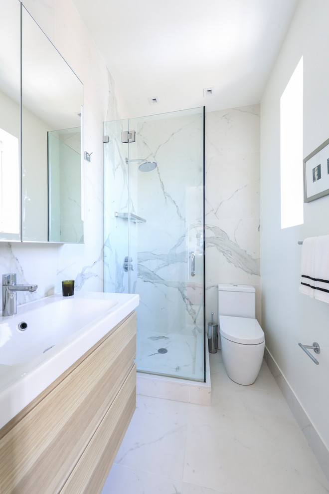 Inspiration for a small contemporary master bathroom in New York with flat-panel cabinets, beige cabinets, a corner shower, a one-piece toilet, white tile, marble, white walls, marble floors, solid surface benchtops, white floor, a hinged shower door, white benchtops and an integrated sink.