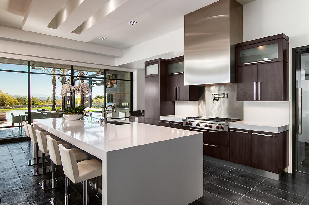 Inspiration for a contemporary galley kitchen remodel in Phoenix with an undermount sink, flat-panel cabinets, dark wood cabinets, metallic backsplash, stainless steel appliances, white walls and an island