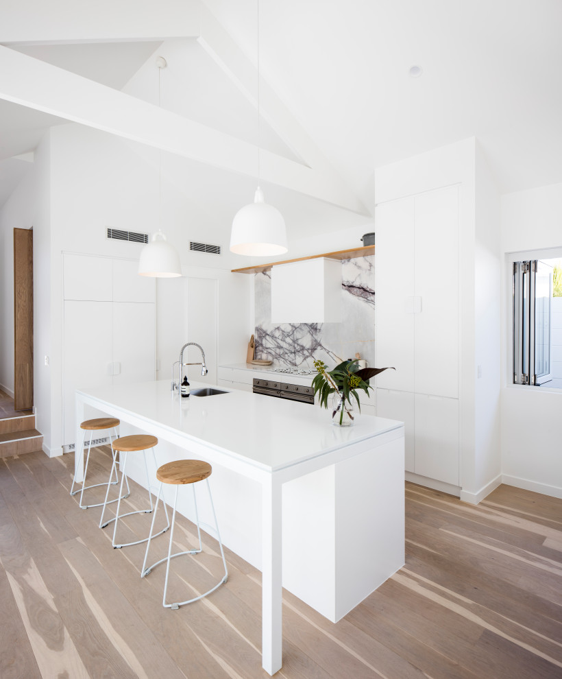Inspiration for a modern galley open plan kitchen in Sunshine Coast with an undermount sink, white cabinets, quartz benchtops, white splashback, marble splashback, panelled appliances, light hardwood floors, with island and white benchtop.