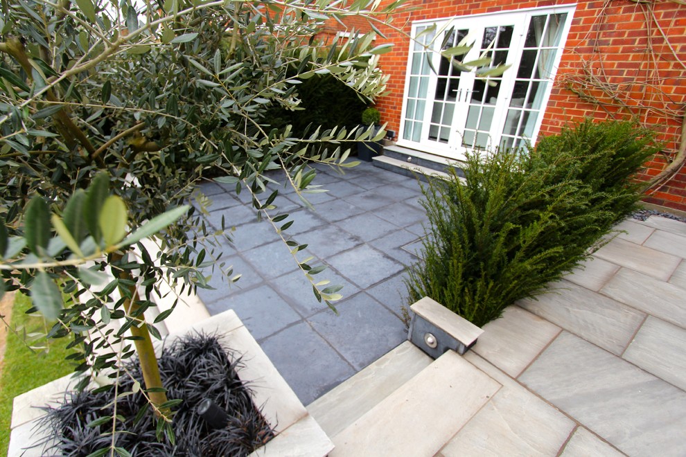 This is an example of a large contemporary backyard patio in Essex with natural stone pavers.
