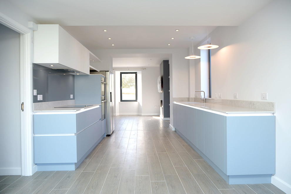 Photo of a mid-sized contemporary open plan kitchen in Cornwall with flat-panel cabinets, blue cabinets, quartz benchtops, grey splashback, glass sheet splashback, stainless steel appliances and grey benchtop.
