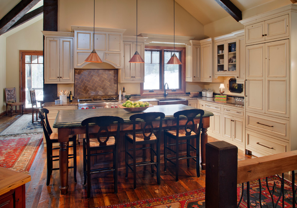 Photo of a mid-sized traditional l-shaped open plan kitchen in Denver with a farmhouse sink, recessed-panel cabinets, beige cabinets, stainless steel appliances, medium hardwood floors, with island, granite benchtops, brown splashback, stone tile splashback, brown floor and brown benchtop.