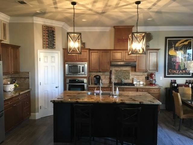 Open concept kitchen - small transitional galley laminate floor and brown floor open concept kitchen idea with an undermount sink, raised-panel cabinets, medium tone wood cabinets, granite countertops, beige backsplash, stone tile backsplash, stainless steel appliances and an island