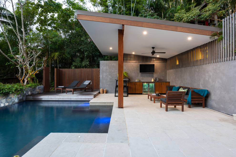 Photo of a large tropical backyard custom-shaped infinity pool in Sunshine Coast with a pool house and natural stone pavers.