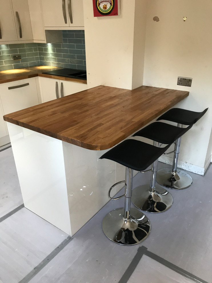Large modern l-shaped kitchen/diner in London with open cabinets, white cabinets, an island, a built-in sink, wood worktops, white splashback, ceramic splashback and ceramic flooring.