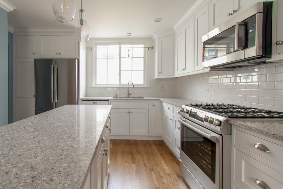 This is an example of a mid-sized transitional l-shaped eat-in kitchen in Milwaukee with an undermount sink, beaded inset cabinets, white cabinets, quartz benchtops, white splashback, subway tile splashback, stainless steel appliances, medium hardwood floors, with island, brown floor and beige benchtop.