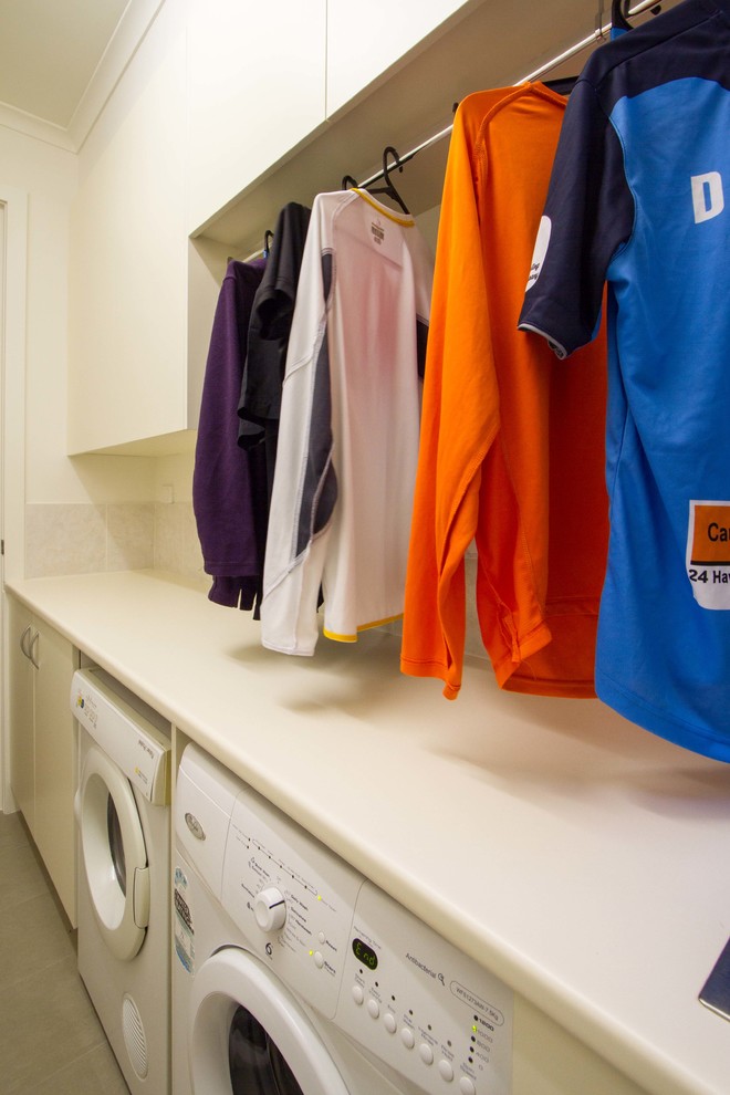 This is an example of a mid-sized modern galley dedicated laundry room in Melbourne with a single-bowl sink, flat-panel cabinets, white cabinets, laminate benchtops and a side-by-side washer and dryer.