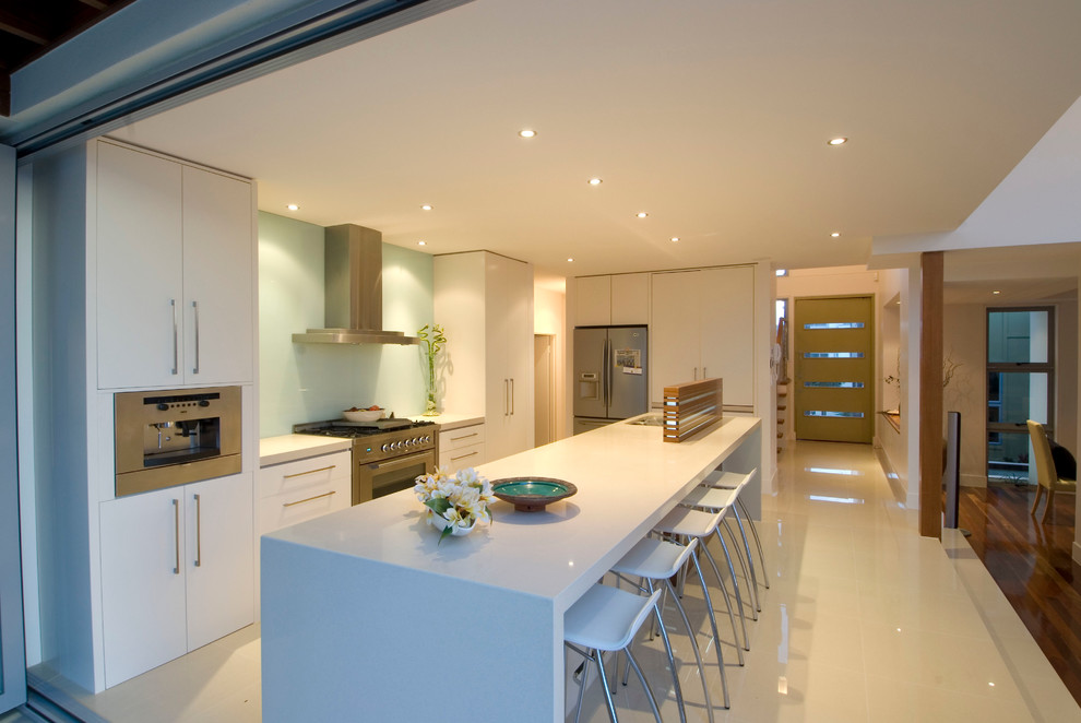Inspiration for a mid-sized contemporary eat-in kitchen in Gold Coast - Tweed with a drop-in sink, flat-panel cabinets, white cabinets, solid surface benchtops, blue splashback, glass tile splashback, stainless steel appliances, porcelain floors and with island.
