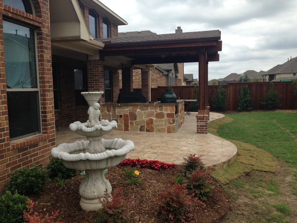 This is an example of a mid-sized country backyard patio in Dallas with stamped concrete, an outdoor kitchen and an awning.