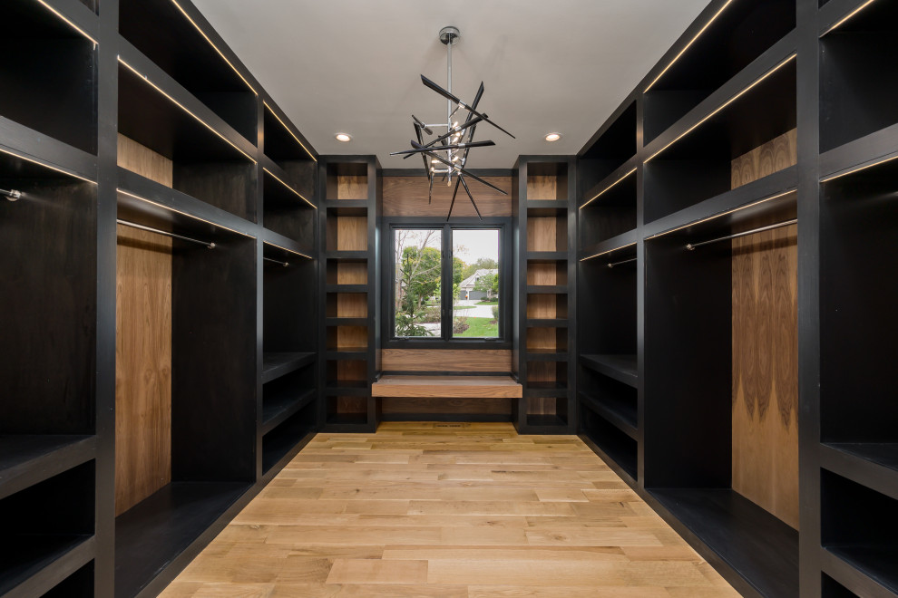 Design ideas for a large modern walk-in wardrobe in Kansas City with black cabinets and light hardwood floors.