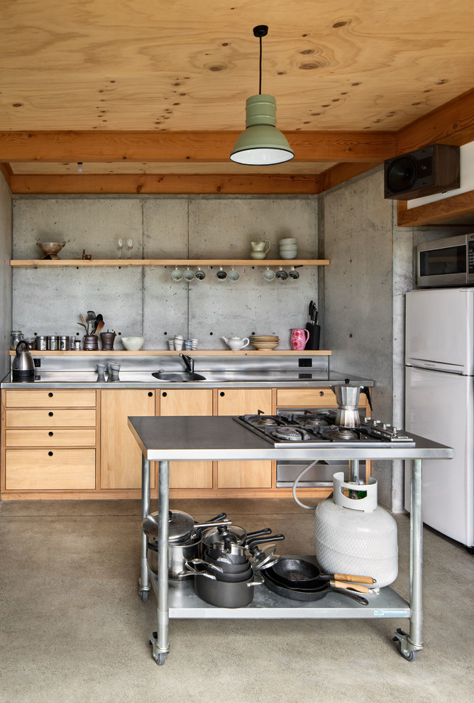 This is an example of a small industrial kitchen in Wellington with flat-panel cabinets, light wood cabinets, stainless steel benchtops and white appliances.