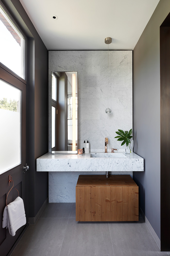Mid-sized contemporary master wet room bathroom in London with medium wood cabinets, a drop-in tub, a one-piece toilet, gray tile, marble, grey walls, porcelain floors, a wall-mount sink, marble benchtops, grey floor, an open shower and flat-panel cabinets.