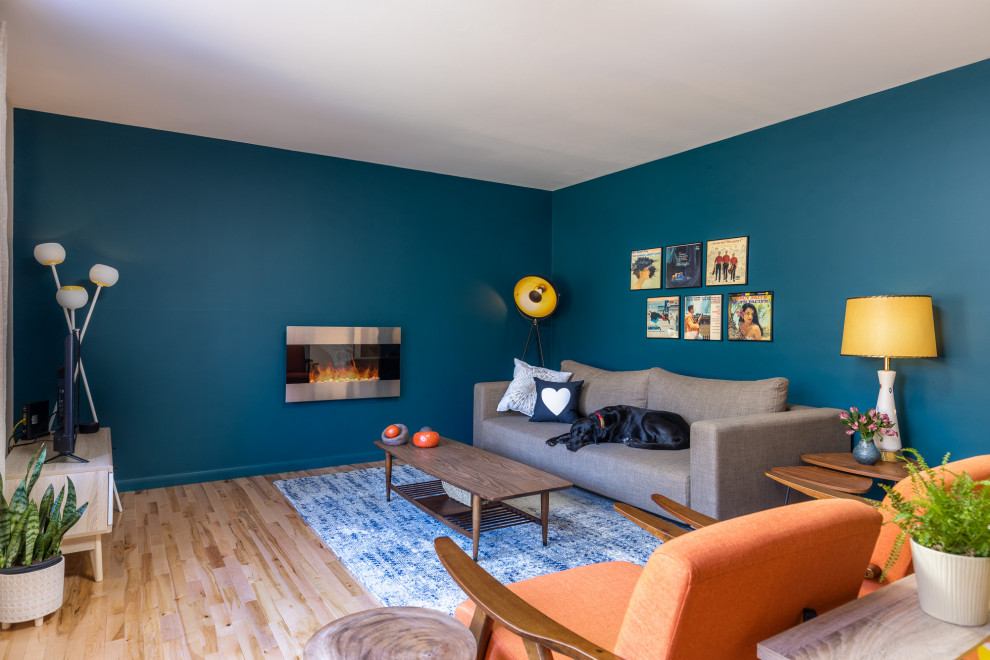 На фото: изолированная гостиная комната среднего размера в стиле ретро с синими стенами, светлым паркетным полом, подвесным камином, фасадом камина из металла, отдельно стоящим телевизором и бежевым полом с