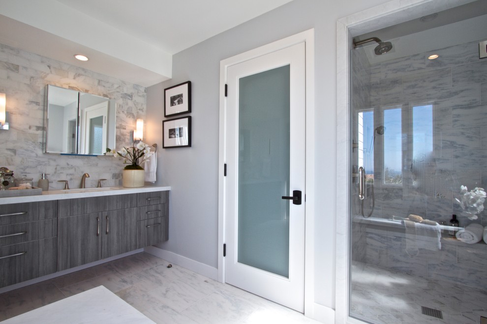 Photo of a mid-sized transitional master bathroom in Orange County with flat-panel cabinets, grey cabinets, a drop-in tub, an alcove shower, a two-piece toilet, gray tile, white tile, subway tile, grey walls, marble floors, an undermount sink and marble benchtops.