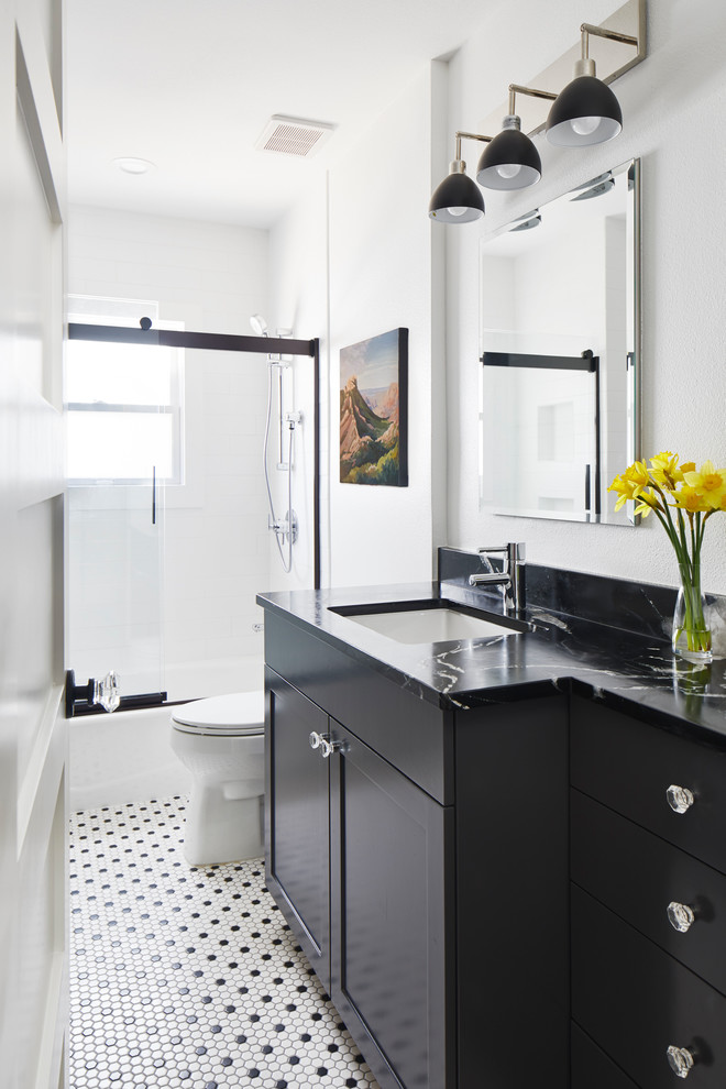 This is an example of a small eclectic kids bathroom in Austin with shaker cabinets, black cabinets, an alcove tub, a shower/bathtub combo, a one-piece toilet, white tile, ceramic tile, white walls, ceramic floors, an undermount sink, soapstone benchtops, white floor, a sliding shower screen and black benchtops.