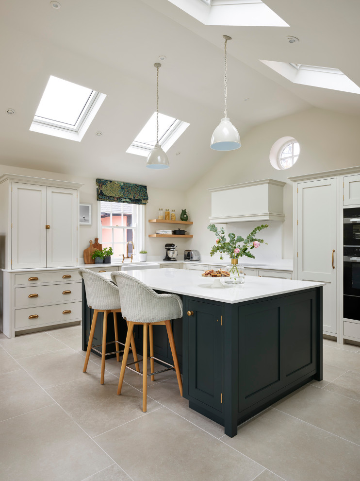 Design ideas for a traditional kitchen/diner in Essex with a belfast sink, shaker cabinets, green cabinets, quartz worktops, white splashback, black appliances, porcelain flooring, an island, grey floors, white worktops and a vaulted ceiling.