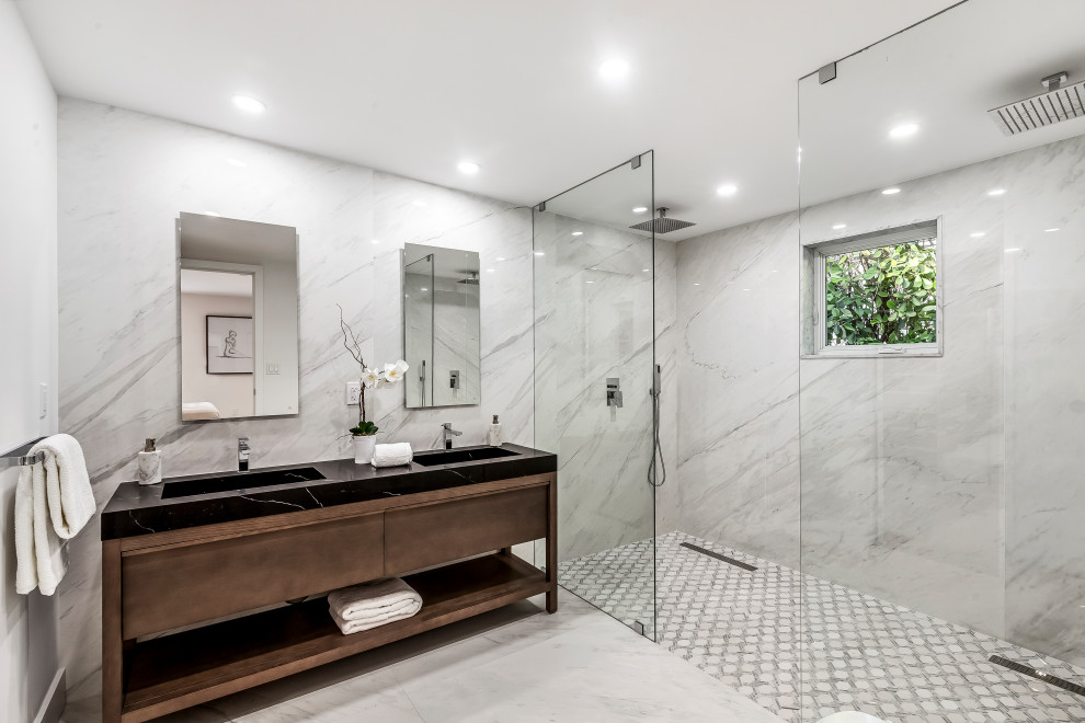 Photo of a large contemporary master bathroom in Miami with dark wood cabinets, a double shower, a one-piece toilet, white tile, marble, white walls, marble floors, marble benchtops, white floor, an open shower, black benchtops, a double vanity and a freestanding vanity.