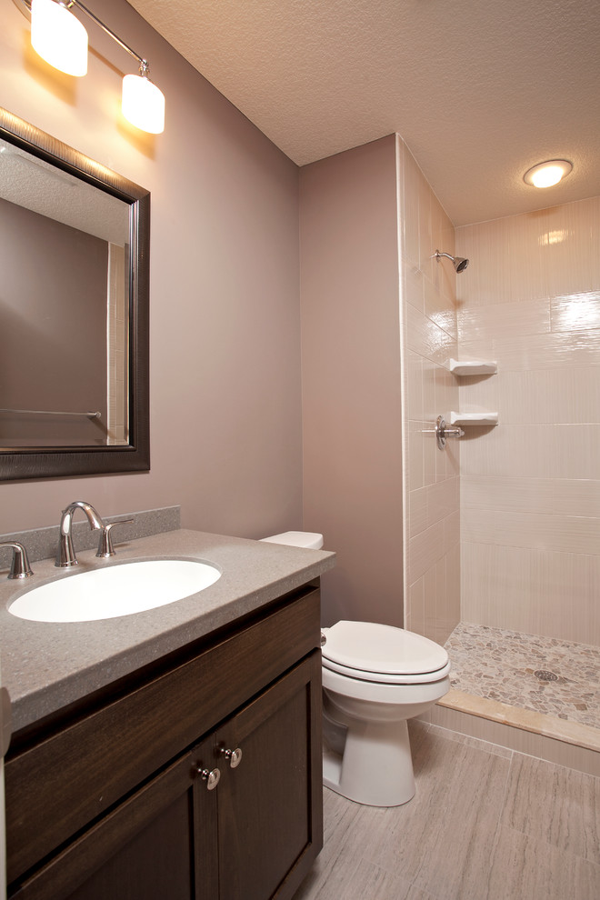 Photo of a mid-sized traditional 3/4 bathroom in Minneapolis with an integrated sink, recessed-panel cabinets, medium wood cabinets, solid surface benchtops, an alcove shower, a one-piece toilet, beige tile, ceramic tile, brown walls and ceramic floors.