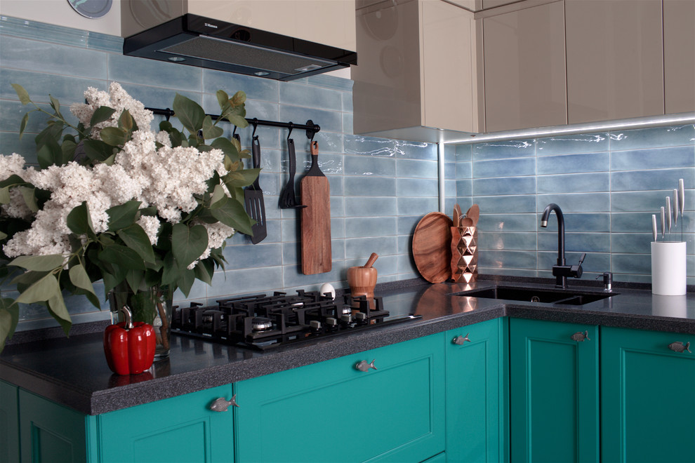 This is an example of a mid-sized beach style l-shaped separate kitchen in Other with an undermount sink, raised-panel cabinets, turquoise cabinets, solid surface benchtops, blue splashback, ceramic splashback, black appliances, porcelain floors, no island, grey floor and grey benchtop.