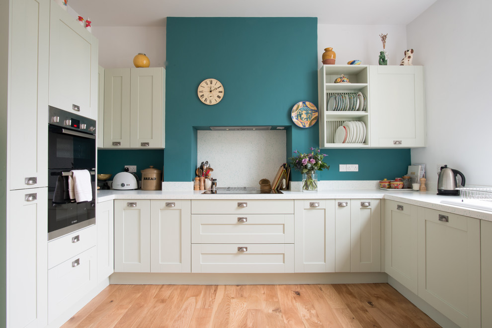 Inspiration for a mid-sized traditional u-shaped kitchen in Other with a double-bowl sink, shaker cabinets, solid surface benchtops, white splashback, panelled appliances, light hardwood floors and no island.