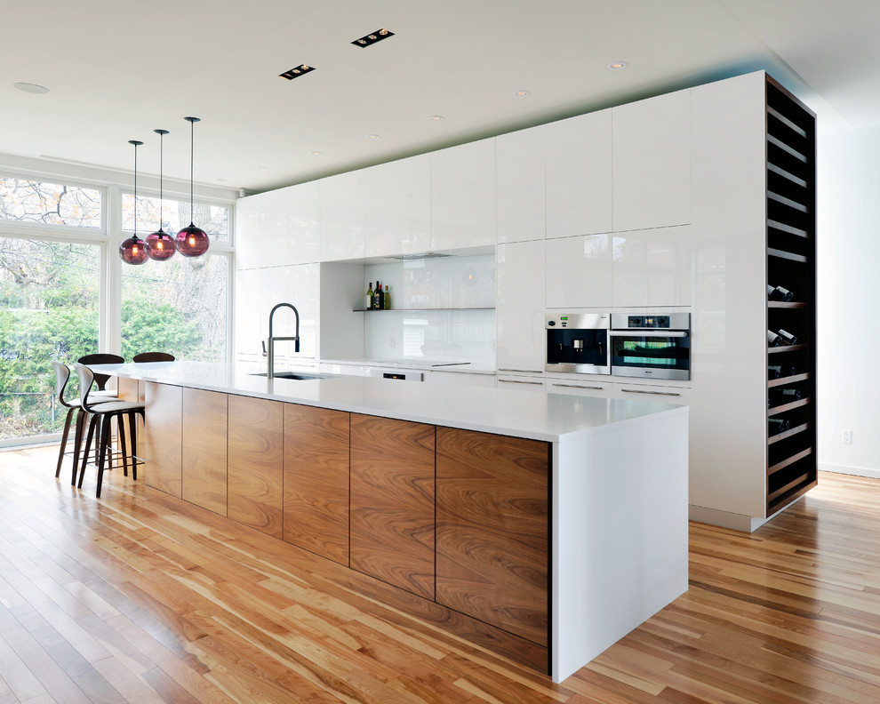 Inspiration for a contemporary galley kitchen in Ottawa with an undermount sink, flat-panel cabinets, white cabinets, white splashback, glass sheet splashback, stainless steel appliances, medium hardwood floors and with island.