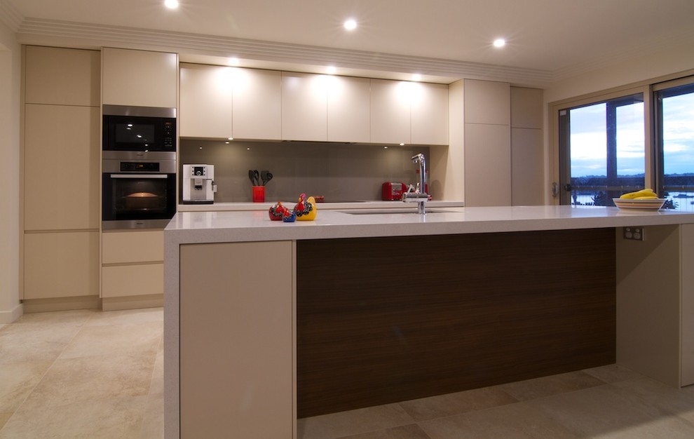 Photo of a mid-sized contemporary galley open plan kitchen in Sydney with an undermount sink, flat-panel cabinets, beige cabinets, quartz benchtops, brown splashback, glass sheet splashback, stainless steel appliances, travertine floors, with island, beige floor and beige benchtop.