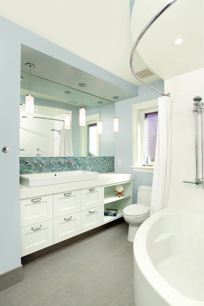 Contemporary bathroom in Toronto with a trough sink, flat-panel cabinets, white cabinets, quartzite benchtops, a corner tub, a shower/bathtub combo, a one-piece toilet, multi-coloured tile, glass tile, blue walls and porcelain floors.