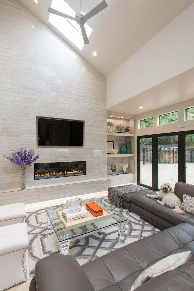 This is an example of a large modern family room in Houston with beige walls, travertine floors, a standard fireplace, a tile fireplace surround and a wall-mounted tv.