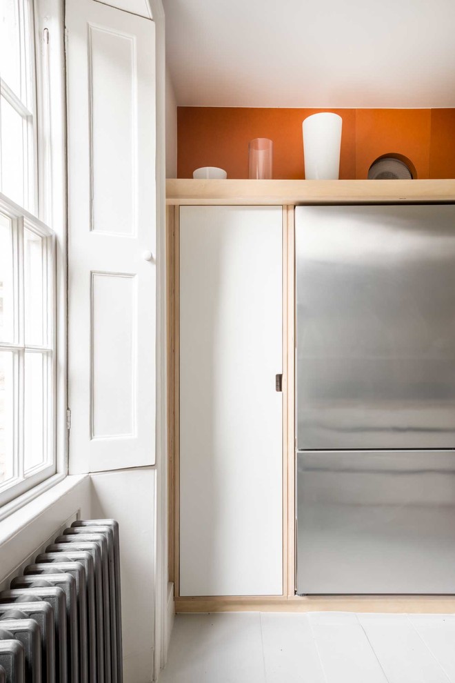 This is an example of a mid-sized contemporary u-shaped separate kitchen in Other with flat-panel cabinets, white cabinets, stainless steel benchtops, stainless steel appliances, light hardwood floors, with island, white floor, a drop-in sink and orange splashback.
