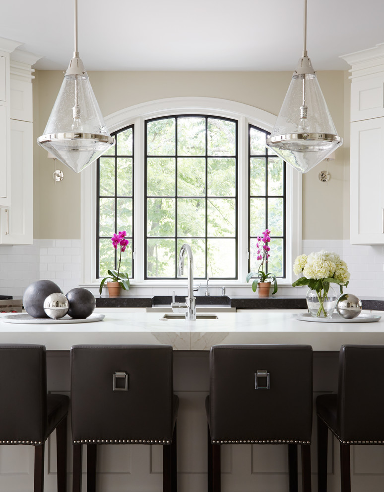 Inspiration for a large transitional u-shaped eat-in kitchen in Chicago with a farmhouse sink, shaker cabinets, white cabinets, white splashback, subway tile splashback, with island, solid surface benchtops and stainless steel appliances.