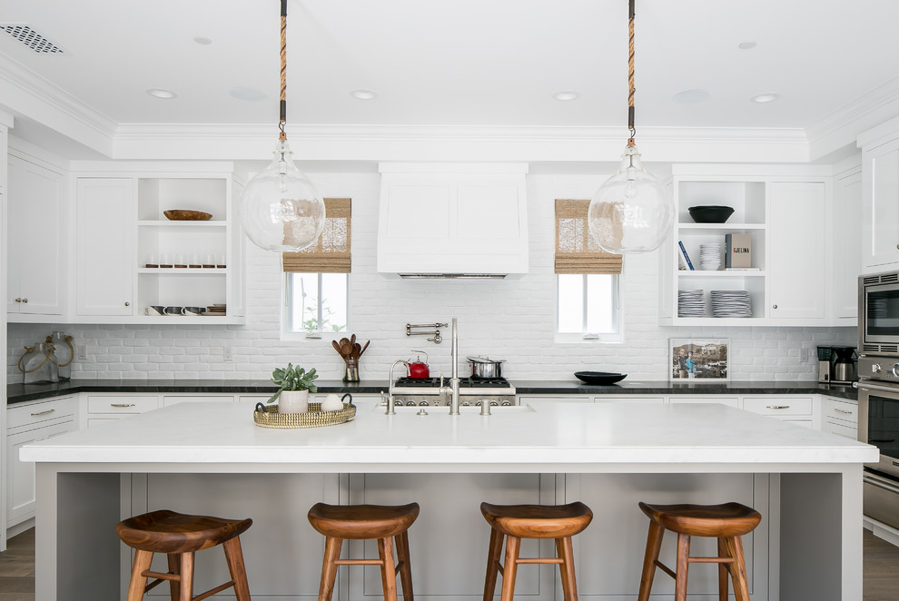This is an example of a beach style u-shaped kitchen in Orange County with open cabinets, white cabinets, white splashback, brick splashback, stainless steel appliances, dark hardwood floors and with island.