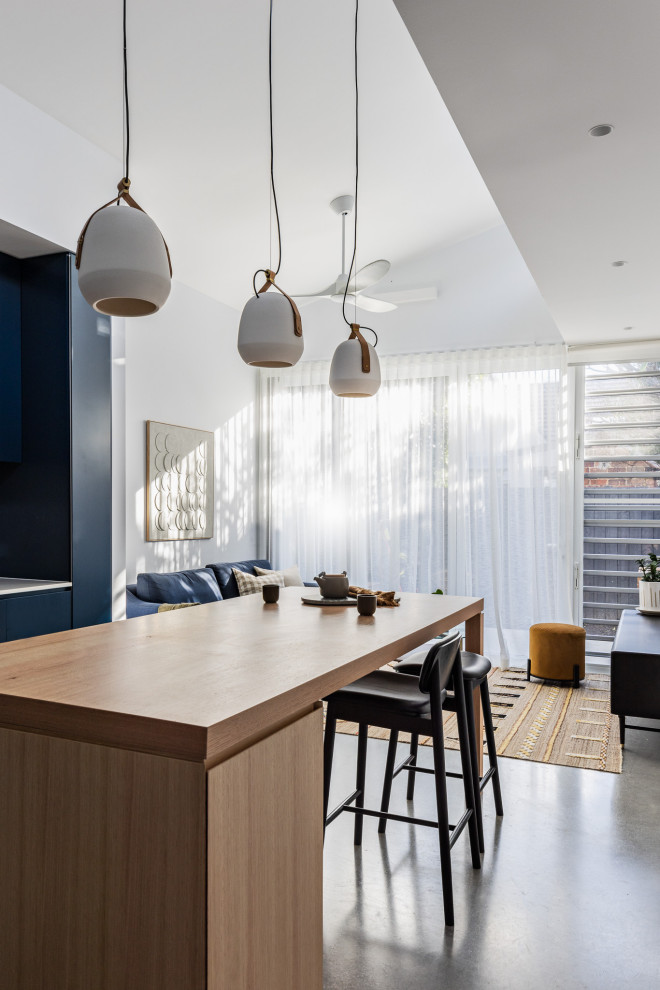 Inspiration for a small contemporary l-shaped eat-in kitchen in Sydney with an undermount sink, blue cabinets, quartz benchtops, white splashback, ceramic splashback, black appliances, concrete floors, with island, grey floor and white benchtop.