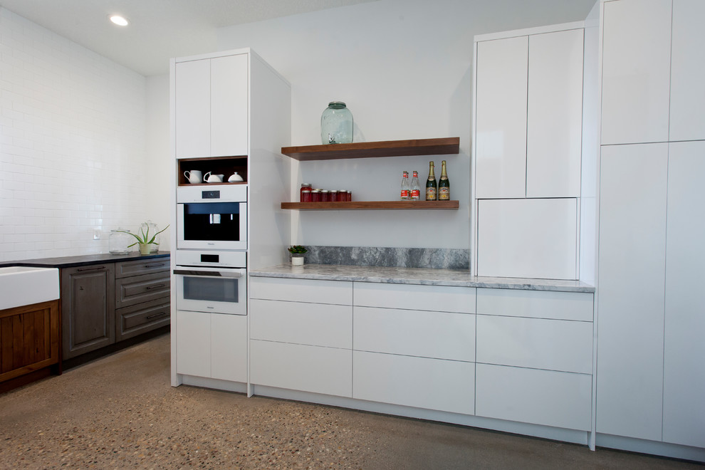 Inspiration for a large modern u-shaped open plan kitchen in Calgary with a farmhouse sink, flat-panel cabinets, white cabinets, white appliances, with island, brown floor and terrazzo floors.