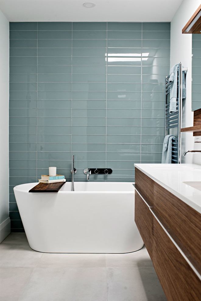 Design ideas for a mid-sized contemporary master bathroom in Toronto with flat-panel cabinets, medium wood cabinets, a freestanding tub, an alcove shower, a wall-mount toilet, blue tile, glass tile, grey walls, ceramic floors, an integrated sink, grey floor, a hinged shower door and white benchtops.