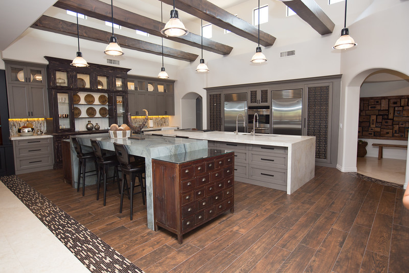 Expansive eclectic u-shaped open plan kitchen in Phoenix with a triple-bowl sink, recessed-panel cabinets, grey cabinets, quartzite benchtops, beige splashback, stone tile splashback, stainless steel appliances, dark hardwood floors and multiple islands.