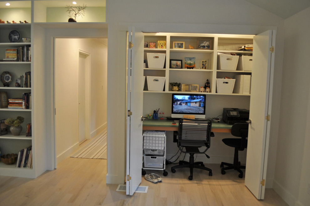 This is an example of a small midcentury study room in Boston with white walls, light hardwood floors and a built-in desk.
