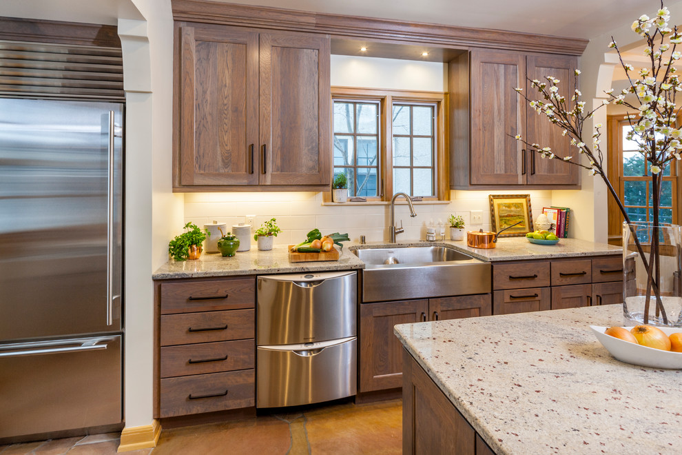 Mid-sized transitional kitchen in Minneapolis with a farmhouse sink, shaker cabinets, medium wood cabinets, granite benchtops, white splashback, subway tile splashback, stainless steel appliances, with island and brown floor.