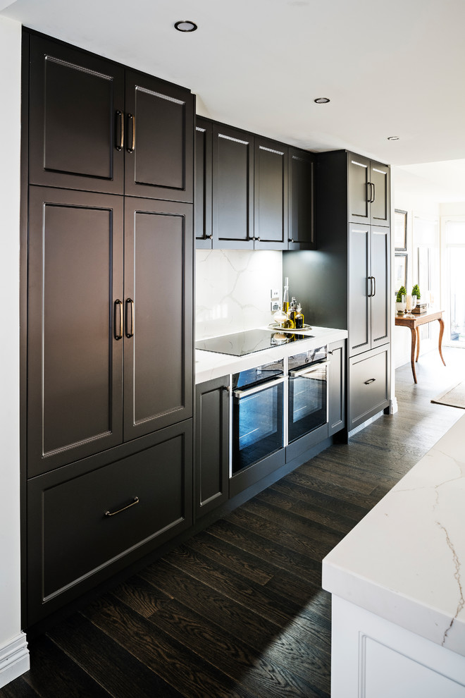 Photo of a large transitional galley open plan kitchen in Melbourne with a double-bowl sink, recessed-panel cabinets, brown cabinets, quartz benchtops, white splashback, stone slab splashback, black appliances, dark hardwood floors, with island, brown floor and white benchtop.