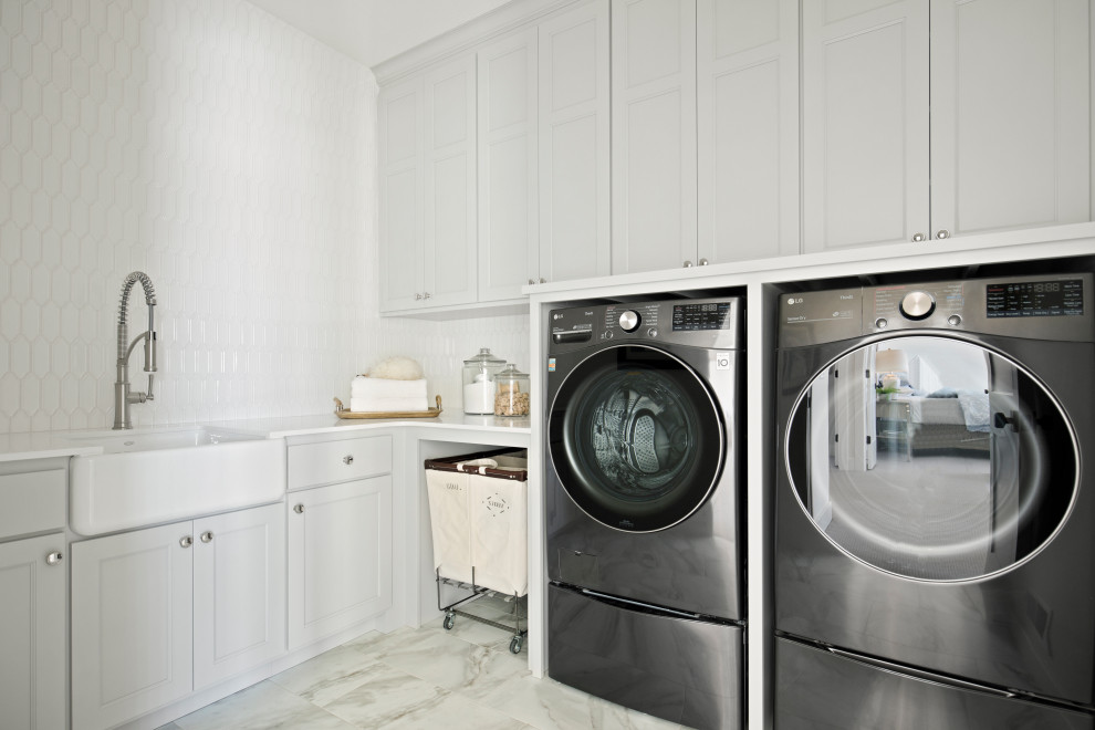 Inspiration for a transitional l-shaped dedicated laundry room in Minneapolis with a farmhouse sink, grey cabinets, white splashback, white walls, a side-by-side washer and dryer and white benchtop.