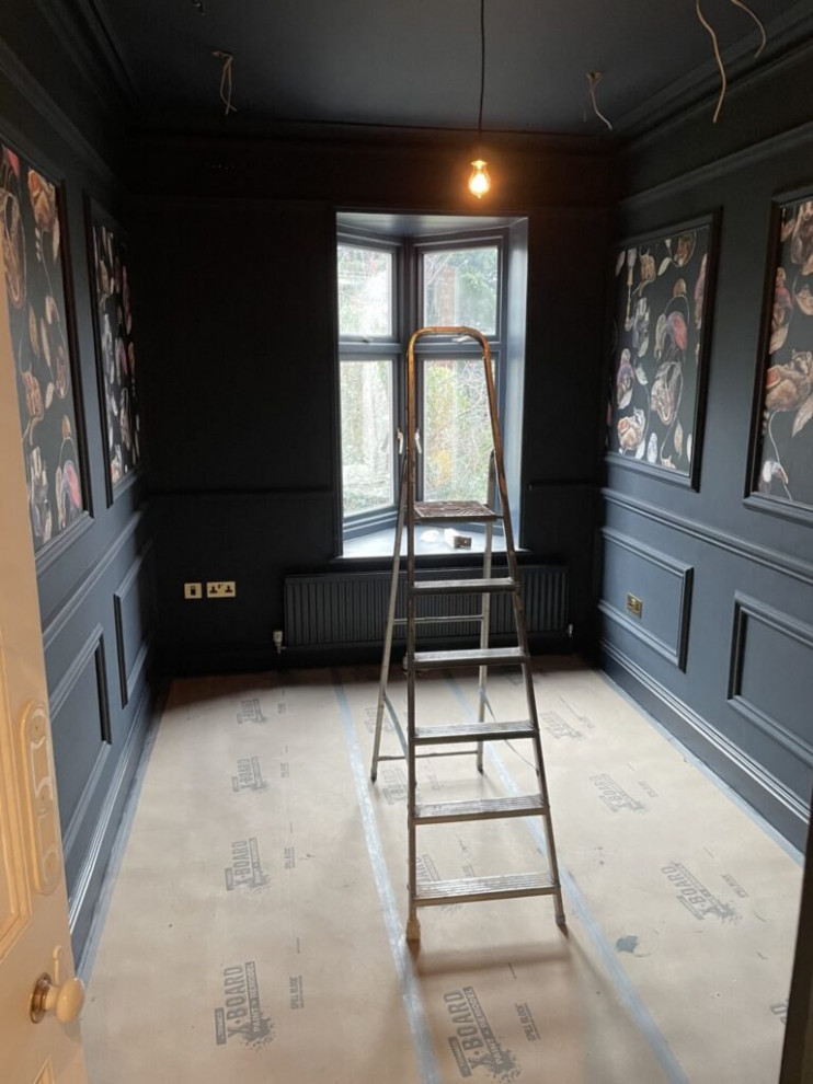 This is an example of a mid-sized guest bedroom in London with black walls, ceramic floors, no fireplace, a concrete fireplace surround, beige floor, wood and decorative wall panelling.