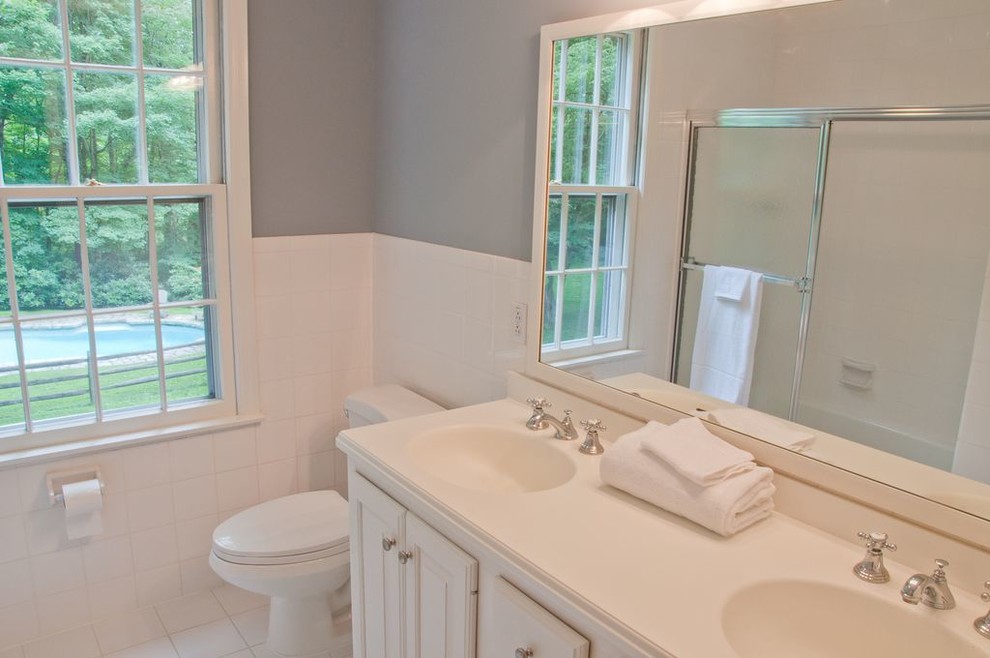 Mid-sized traditional master bathroom in New York with raised-panel cabinets, white cabinets, white tile, ceramic tile, grey walls, ceramic floors, an integrated sink, laminate benchtops, white floor, white benchtops, an alcove tub, a shower/bathtub combo, a two-piece toilet and a sliding shower screen.