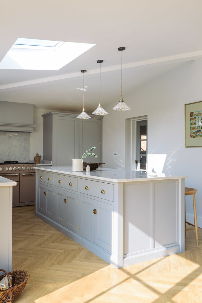 Large transitional l-shaped open plan kitchen in Other with a farmhouse sink, shaker cabinets, grey cabinets, marble benchtops, white splashback, marble splashback, coloured appliances, light hardwood floors and with island.