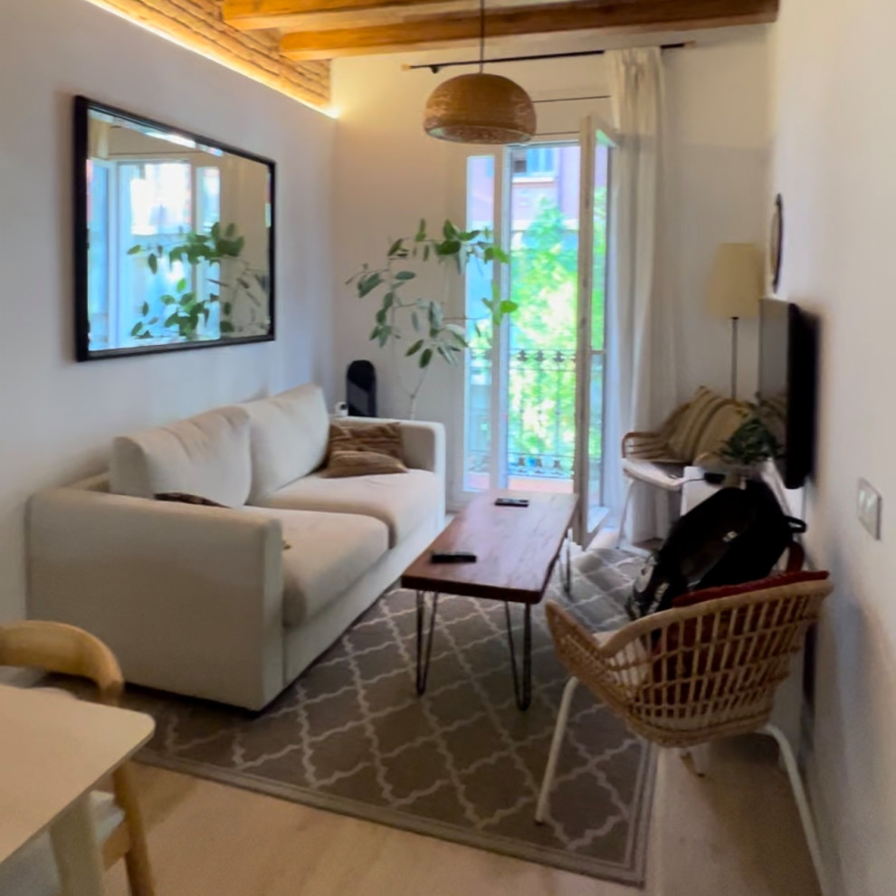 Пример оригинального дизайна: маленькая открытая гостиная комната в белых тонах с отделкой деревом в средиземноморском стиле с белыми стенами, светлым паркетным полом, отдельно стоящим телевизором, коричневым полом, балками на потолке, кирпичными стенами и красивыми шторами для на участке и в саду