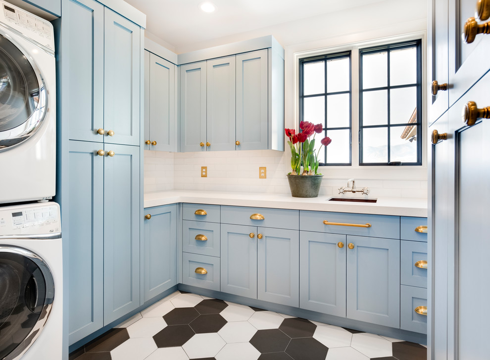 Photo of a transitional u-shaped utility room in Salt Lake City with blue cabinets, white walls, a stacked washer and dryer, multi-coloured floor, an undermount sink, shaker cabinets and white benchtop.