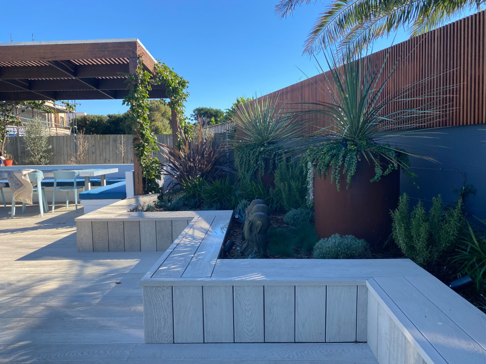 This is an example of a medium sized modern back xeriscape full sun garden in Sydney with a raised bed, decking and a wood fence.