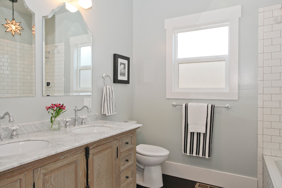 Mid-sized arts and crafts bathroom in San Francisco with a console sink, furniture-like cabinets, distressed cabinets, marble benchtops, a shower/bathtub combo, a two-piece toilet, white tile, porcelain tile, grey walls, dark hardwood floors and an alcove tub.