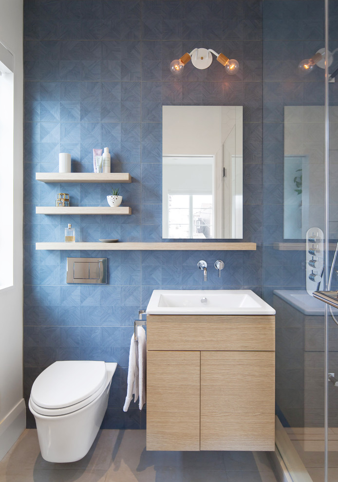 Photo of a contemporary bathroom in Toronto with flat-panel cabinets, white walls, engineered quartz benchtops, light wood cabinets, an alcove shower, a wall-mount toilet, blue tile and a console sink.