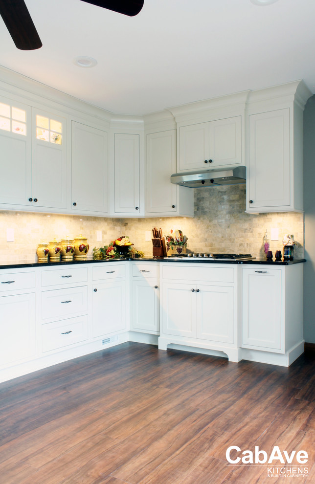 Example of a mid-sized transitional l-shaped vinyl floor and brown floor eat-in kitchen design with an undermount sink, recessed-panel cabinets, white cabinets, quartz countertops, beige backsplash, ceramic backsplash, stainless steel appliances and no island